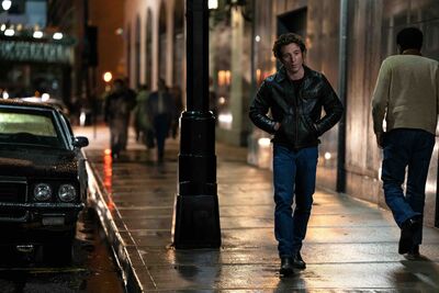 A man in a leather jacket walks down a rainy street at night