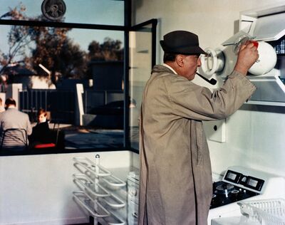 A man smokes a pipe and tries to operate a modern-looking machine.