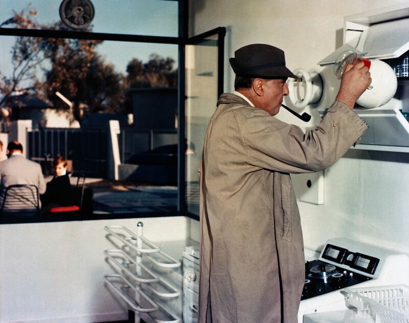 A man smokes a pipe and tries to operate a modern-looking machine.