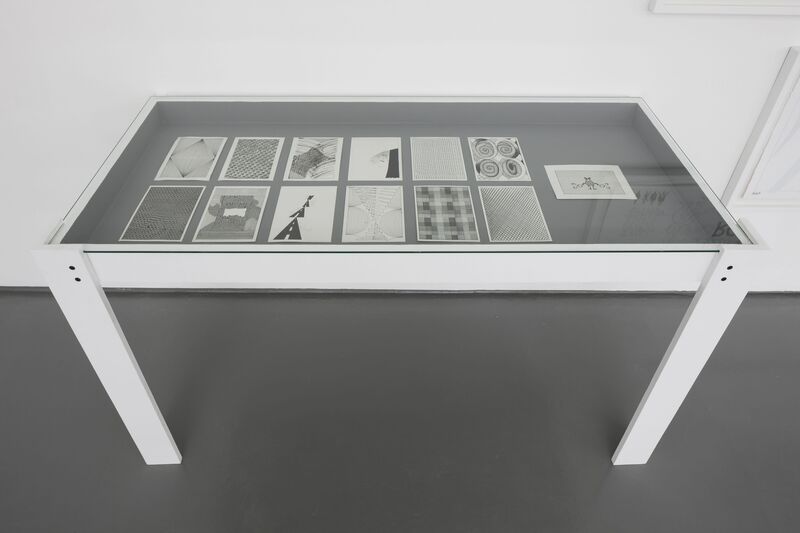 From Continue Without Losing Consciousness, a white glass table displays 10 A5 black-and-white pencil drawings of abstract patterns.