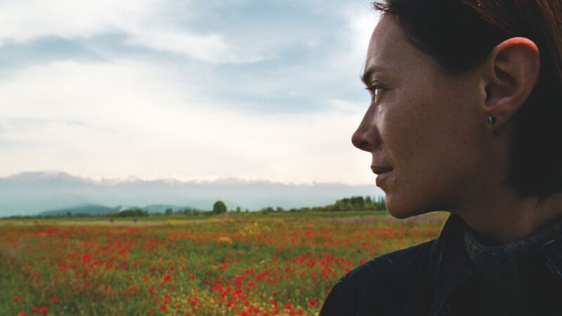 A woman looks out at a poppy field.