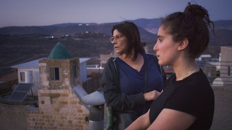 Two women stand on a roof looking at the distance.