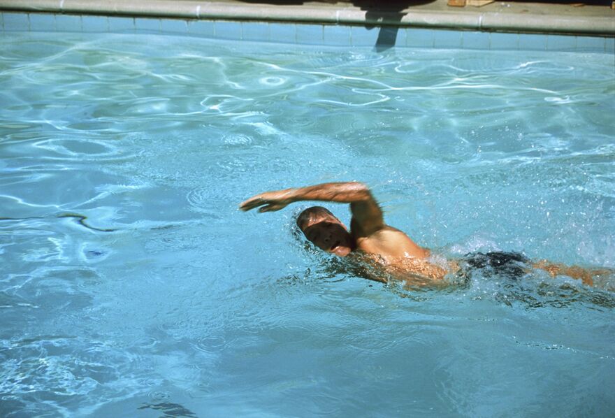 A man swims in a bright blue pool
