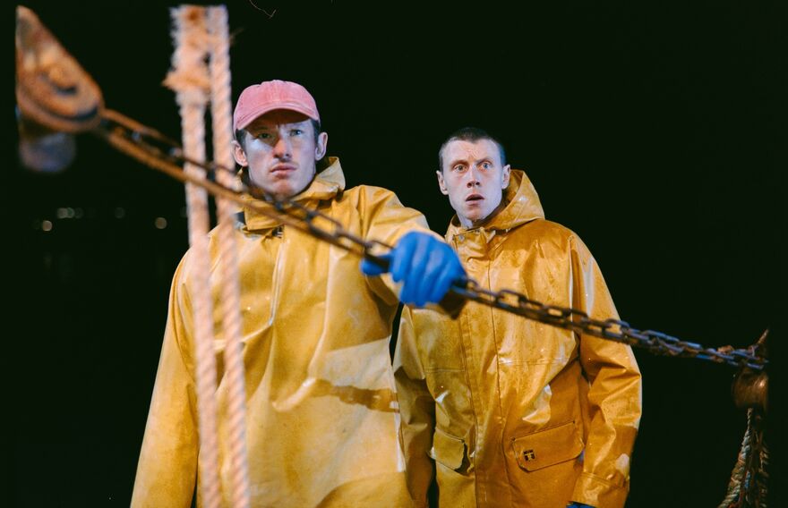 Two men in yellow waterproof jackets on a fishing vessel.