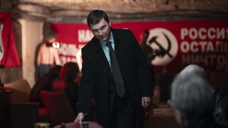 A man in a suit and tie sits down in a dark room. 