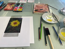 Table covered in paints and brushes and an image of a sunflower