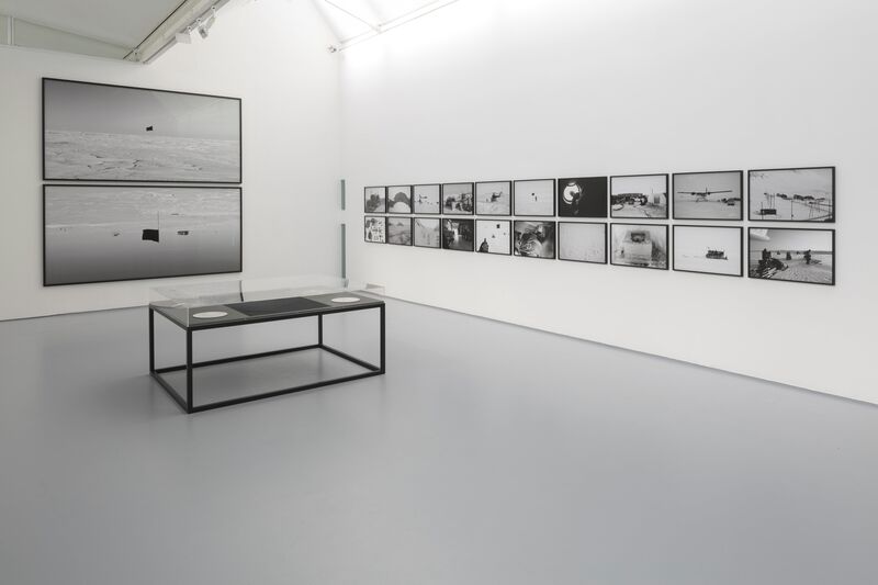 From Santiago Sierra's exhibition 'Black Flag'.black and white photography in black frames on white walls. Two large photographs show black flags against snowy backdrops.