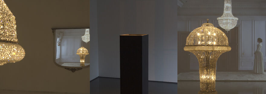 Works by Matthew Buckingham - a golden, sparkling chandelier reflected in a mirror, a black plinth, and the same chandelier again, this time in a room with a woman in early 20th-century clothing on.