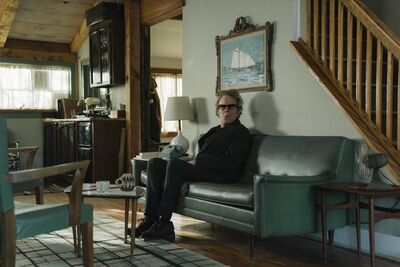 A man in glasses sits alone on his sofa.