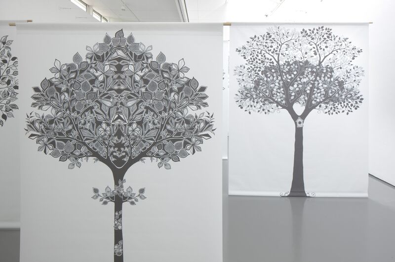 White canvases hang as part of Johanna Basford's exhibition. They are decorated with intricate black pictures of trees, made up of very detailed patterns.