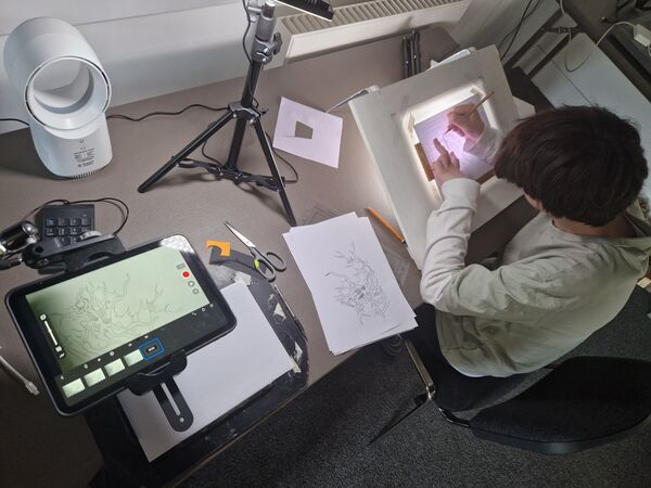 Person at a desk with animation equipment. They are drawing at a lightboc