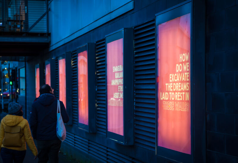 A series of posters illuminated in poster holders on a dark city street