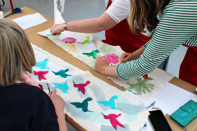 People painting bird and flower designs onto fabric
