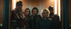 A group of superheroes wearing dark clothes stand in a crowded room.