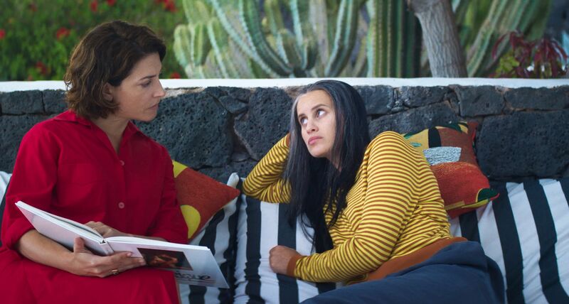 Two women sit on a sofa looking at each other