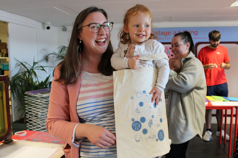 Parent and child smiling as they hold their Hello In Their printed tote bag
