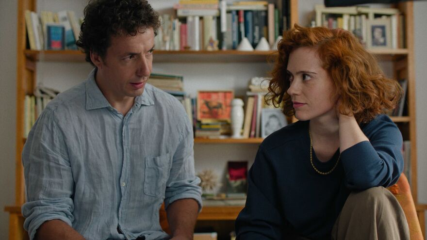 A man and woman sit in a living room looking at each other.