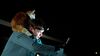 A young man with a headlight torch and a cat on his shoulder takes a picture of something in the distance