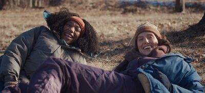 Two young woman lie on the wintry ground and laugh together.