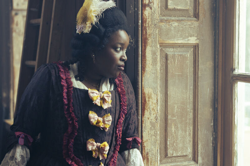A woman in period costume looks out of a window