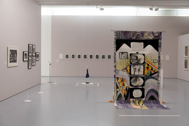 A gallery space with images on the wall and a colourful fabric banner hanging in the centre