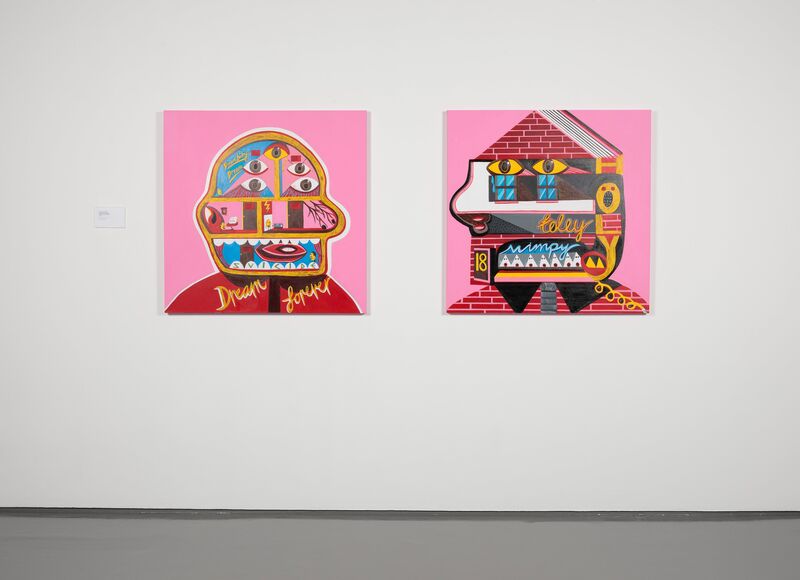 Two paintings on a white wall. Both are surreal images of faces which have been combined with houses. They are against a pink background and use flat but very bright colours.