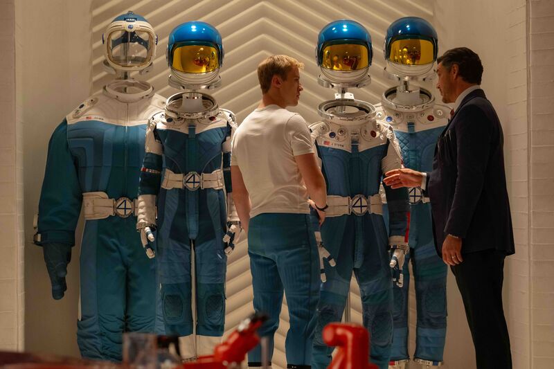 Two people look at a collection of blue and white shiny space suits.