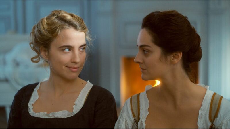 Two woman in historical costume look at one another and smile.