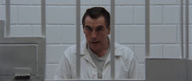 A man sits behind prison bars in a white jumpsuit