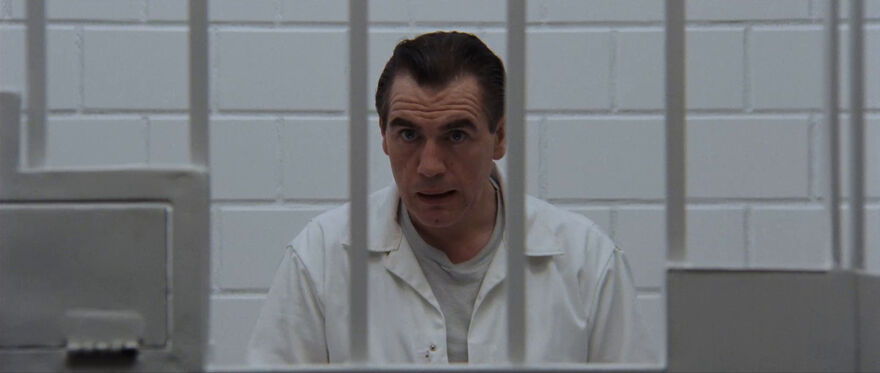 A man sits behind prison bars in a white jumpsuit