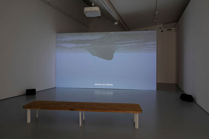 A screen in a gallery a wooden bench in the foreground