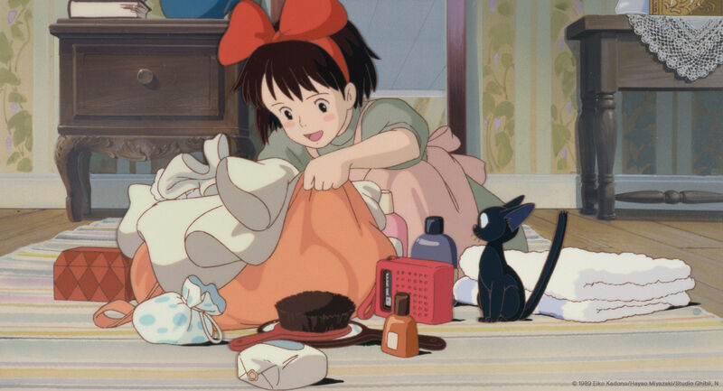 a young girl bundles clothes while watched by a black cat