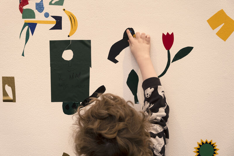 Child sticking vinyl to the wall outside of Gallery 1 to create a giant mural