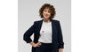 A white woman with curly hair stands looking at the camera with her hand on her hip 