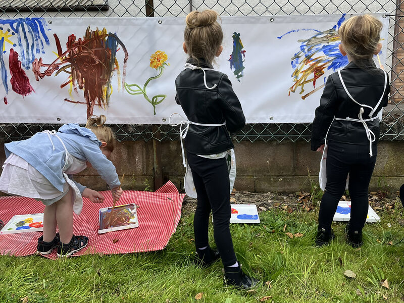 Three children painting on a banner tied to a fence