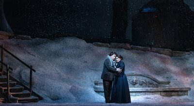 A man and woman embrace on a stage filled with snow