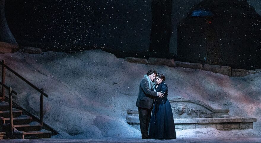 A man and woman embrace on a stage filled with snow