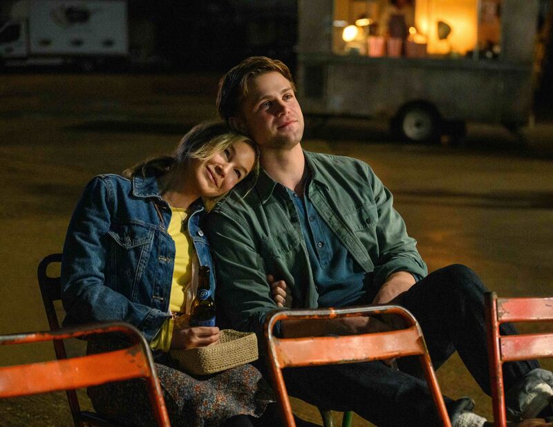 A man and a woman sit on folded chairs, the woman has her head on his shoulders.