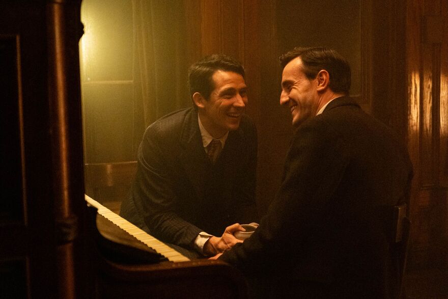 Two men wearing 1910s clothing laugh together.