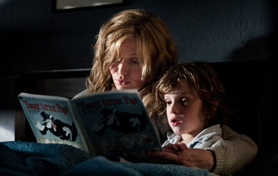 A woman and a little boy read a book together in bed.