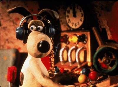 A startled Gromit sits at a control panel wearing headphones