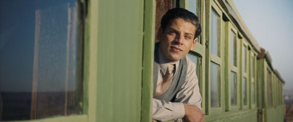 A man in 1930s clothing leans out of a train window