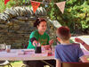 Artist tutor in a Playful Gardens t-shirt at a table with a family painting