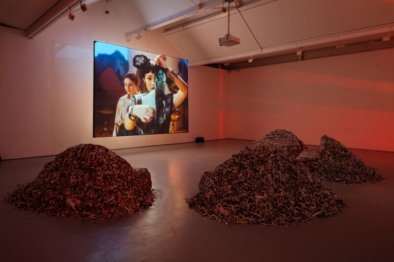 A large video screen in a gallery, showing an actor playing Hollywood star Anna May Wong ripping up a photograph of herself. 