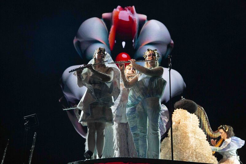 Three flautists perform on stage wearing unusual, avant-garde costumes.