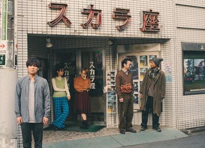 A group of 5 people stand outside of a white tiled building with Japanese lettering on it.